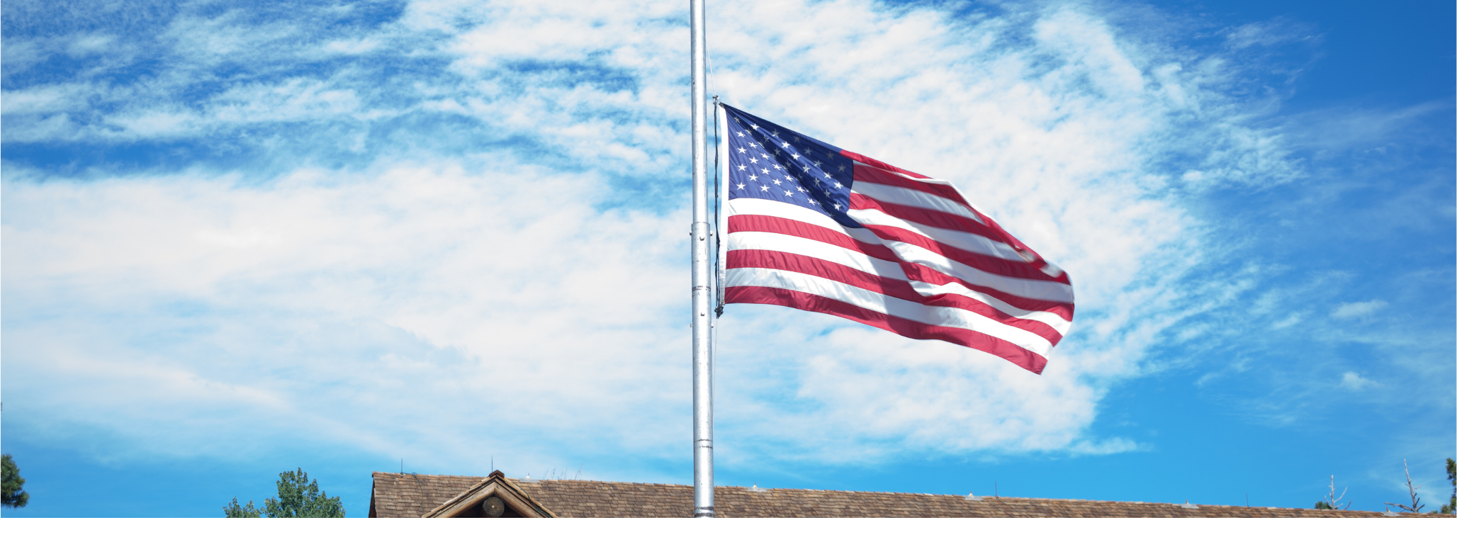 American flag at half-staff on a flagpole against a blue sky